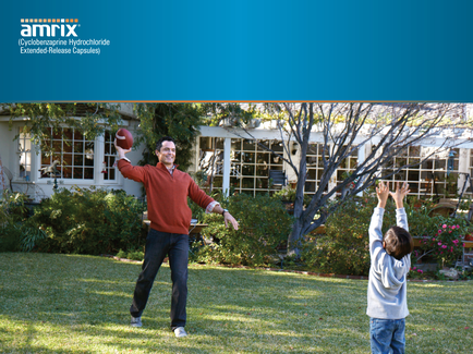 A father and son playing football in a garden. The father is standing on the left side of the image holding a football in his right hand and throwing it towards the son on the right side. He is wearing a red sweater and jeans and has a big smile on his face. The son is standing in front of him with his arms raised in the air reaching up to catch the ball. In the background there is a large white house with a garden and trees. The image appears to be a promotional advertisement for Amrix a company that provides extended-release capsules.