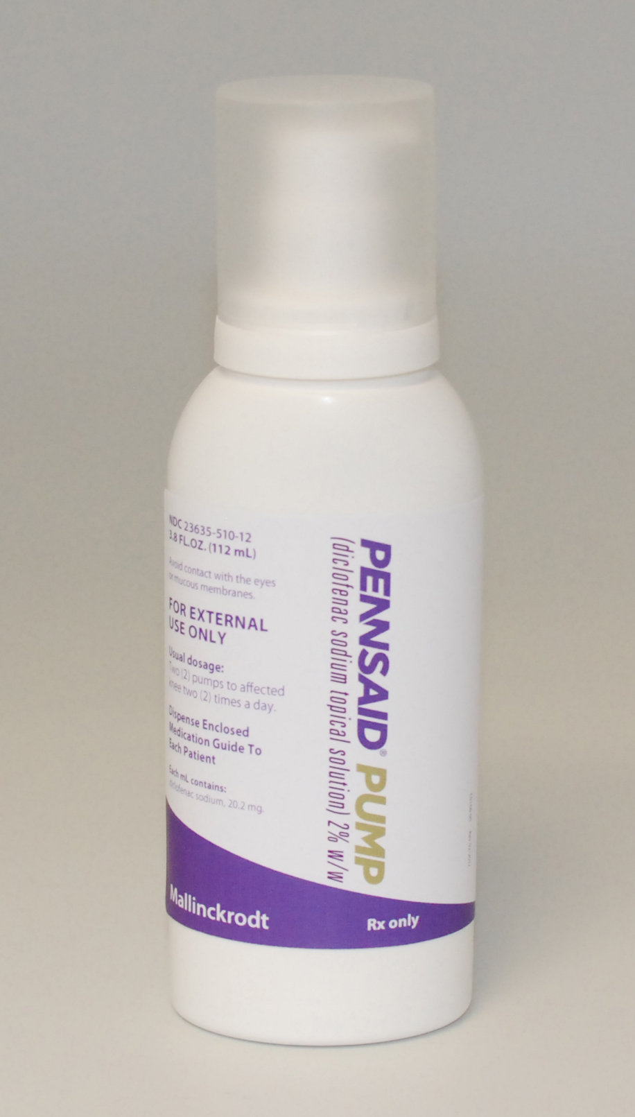 Of a white plastic bottle with a purple label. The label has the brand name "Pennsaid Pump" written in bold black letters at the top followed by the product name "For External Use Only" in smaller black letters. Below that there is a description of the product which states that it is an external use only product. The bottle has a white cap and is standing upright on a plain white background.