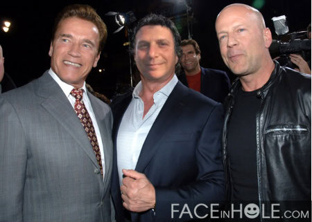 Three men posing together. On the left is Arnold Schwarzenegger and on the right is Bruce Willis.  The man in the middle has had his face photoshopped into the image. In the background there are other people and cameras suggesting that the event is taking place at night. Text at the bottom appears to indicate that the image was created using FaceInHole.com.