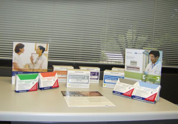 A table with a variety of brochures and pamphlets on it. The table is in an office setting with a window with blinds in the background. On the left side of the table there is a banner with an image of a doctor and a patient. The brochures are in different colors and sizes and some have text and images on them. There is also a brochure with a picture of a man in a white lab coat and a stethoscope on the right side. In the center of the image there are several pamphlets with information about the brochures.