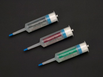 Three syringes of different sizes and shapes. The syringes are arranged in a row on a black background. The first syringe on the left has a blue needle and a silver cap while the second syringe in the middle has a red needle and the third syringe at the bottom has a green cap. All three syringes have the brand name "Optimizer" written on them in white letters.