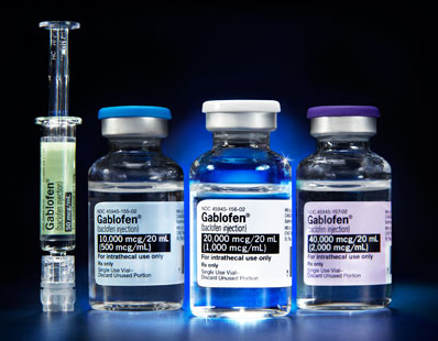 Three vials of Gablofen vaccine. The vials are arranged in a row with the first vial on the left the second vial in the middle and the third vial at the bottom. All three bottles have blue caps and white labels with the brand name and dosage information printed on them. The background is black making the vials and vials stand out. The image appears to be taken in a laboratory setting.