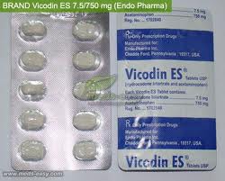 A blister pack of Vicodin ES 7.5/750 mg (Endo Pharma) tablets. The blister pack is white with a blue label on the right side. The label has the brand name "Vicodin" written in bold black letters at the top followed by the product name "ES" in smaller black letters. Below that there is a description of the product which states that the tablets are made in the United States and are used for medical purposes. <br /><br />The blister pack contains 12 tablets each with a round shape and a silver-colored cap. The tablets are arranged in a single blister pack. The pack appears to be new and unused with no visible signs of wear or tear.