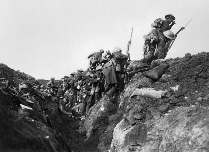 A black and white photograph of a group of soldiers on a hill. The soldiers are wearing helmets and carrying rifles and other military equipment. They are walking up a steep hill with some of them climbing up the side of the hill while others are walking down the slope. The hill appears to be made of dirt and rocks and there are piles of rubble and debris scattered around. The sky is overcast and the overall mood of the image is tense and somber.