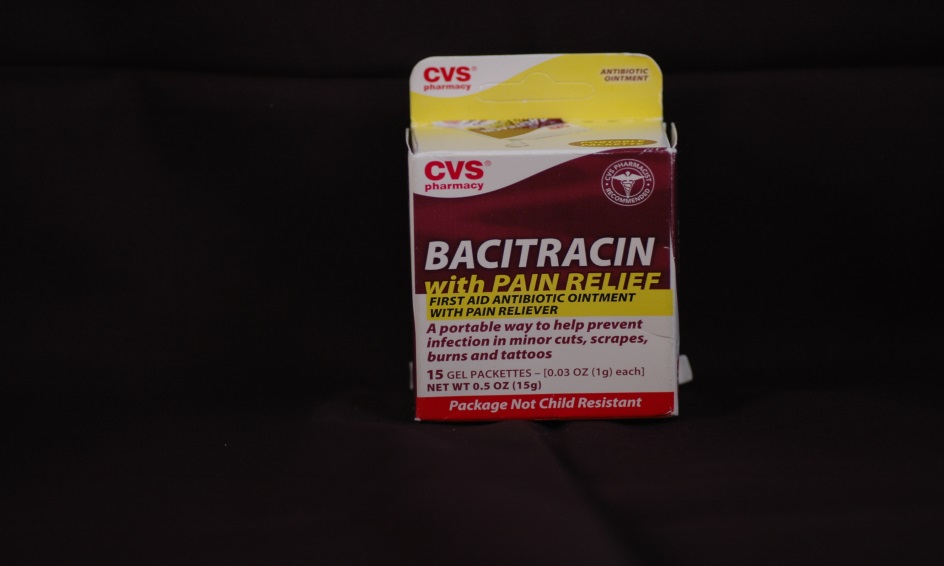 Of a box of CVS Bacitracin with Pain Relief. The box is rectangular in shape and has a red and yellow color scheme. The front of the box has the brand name "CVS" written in bold white letters at the top followed by the product name "BACITRACIN" in smaller white letters. Below that there is a description of the product which states that it is a portable way to help prevent pain relief. The label also mentions that the product is made with natural ingredients and is suitable for children aged 0-3 years old. At the bottom of the label it says "Package Not Child Resistant". The box appears to be unopened and is placed on a black background.