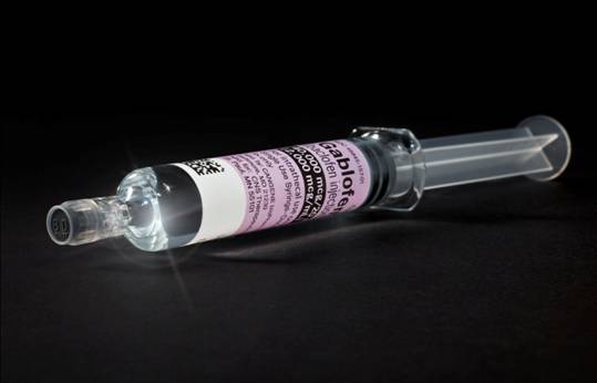 A syringe with a clear plastic body and a transparent cap. The syringe is lying on a black background. The label on the syringe has a pink and white design with the word "Gabor" written in bold letters at the top. Below the label there is a barcode and some information about the product. The cap is slightly tilted to the side and the needle is visible on the right side of the image.