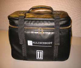 A black leather duffel bag with a handle and two straps on either side. The bag has a zipper on the front and a label on the side that reads "ALLINCRODT". The bag appears to be made of high-quality leather and has a shiny finish. It is sitting on a beige surface.