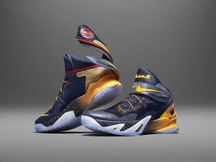 A pair of Nike basketball shoes. The shoes are predominantly blue and yellow in color with a red and yellow accent on the heel. The upper part of the shoe is predominantly navy blue with yellow accents and a white middle. The Nike swoosh logo is visible on the side in red. The laces are also navy blue and the tongue of the sneaker is yellow with a yellow and red design. The middle is white with a black outsole and the outsole is black. The sneakers have a unique design with a combination of blue yellow and red colors. The background is a plain grey color.