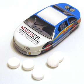 A small tin box with a toy car inside. The tin box is white with a blue and yellow design on the front. The car has the word "MAGNACET" written on it in red and yellow letters. The lid of the tin box has a picture of a race car on it. There are six white pills scattered around the box. The background is plain white.