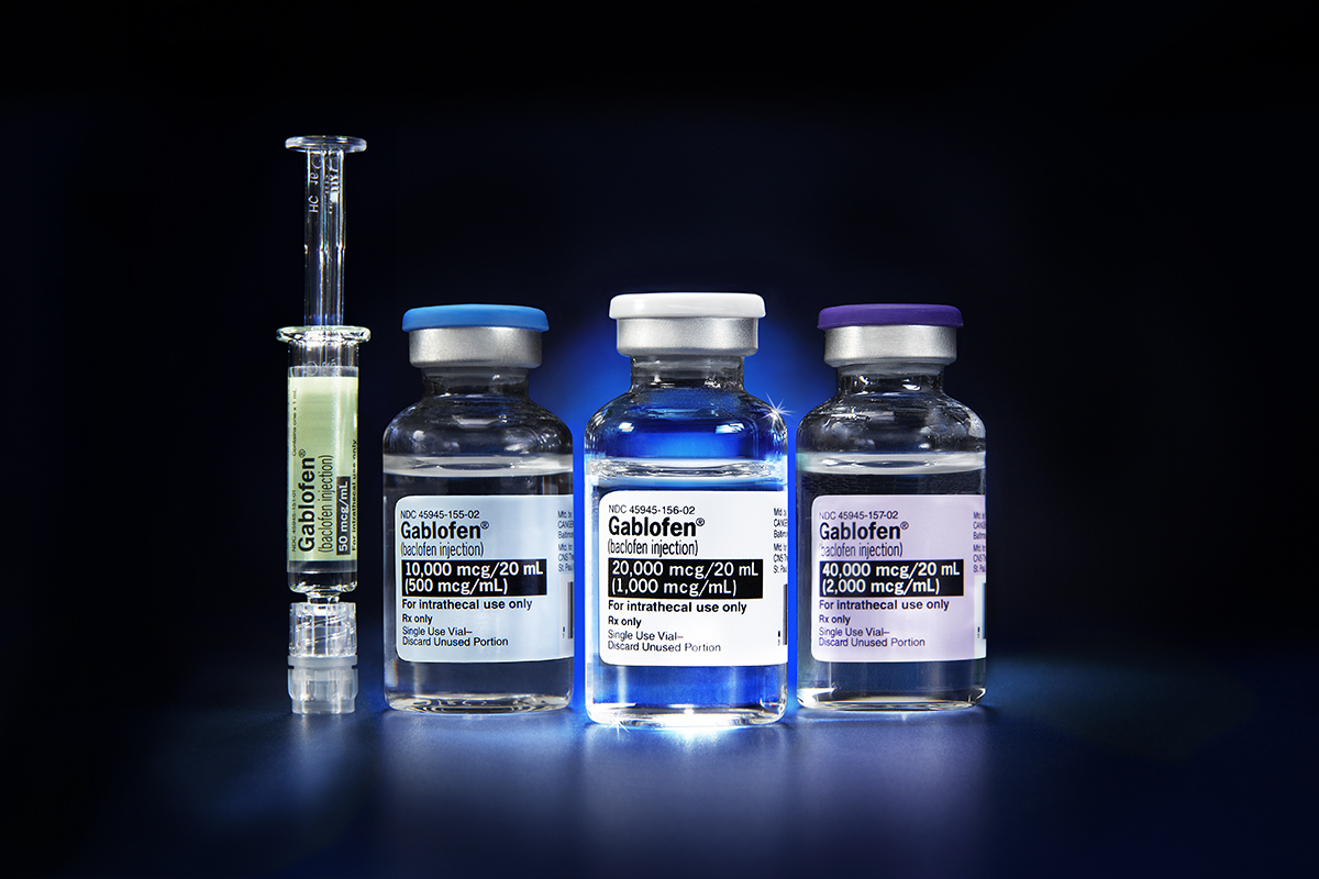 Three small glass vials with blue caps and white labels. The vials are arranged in a row on a dark blue background. On the left side of the image there is a syringe with a green liquid inside. The syringe is filled with a clear liquid and has a needle at the end. Next to the syringe there are two smaller vials one with a blue label and the other with a white label. All three vials appear to be filled with different types of medical supplies.