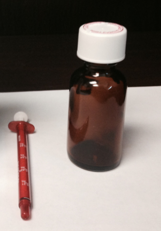 A small brown glass bottle with a white cap. The bottle appears to be empty and is placed on a white surface. Next to the bottle there is a red thermometer with a long handle and a round head. The thermometer is likely used to measure the temperature of the liquid inside the bottle. The background is black making the bottle and thermometer stand out.