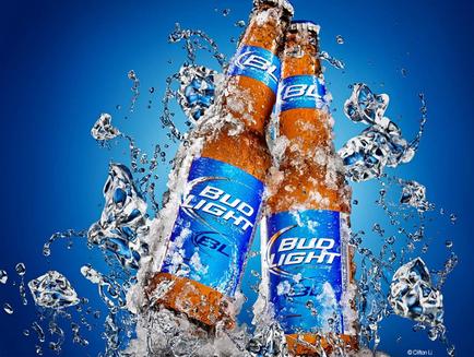 Two bottles of Bud Light beer splashing in the air. The bottles are orange in color and have a blue label with the Bud Light logo on it. The background is a solid blue color and there are several ice cubes scattered around the bottles creating a splash effect. The ice cubes are of different sizes and shapes and they appear to be floating in mid-air. The overall mood of the image is dynamic and energetic.