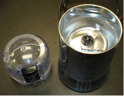 Two objects on a black surface. On the left side there is a small plastic container with a clear lid. The container appears to be made of plastic and has a handle on the top for easy carrying. The lid has a small hole in the center which is likely for the lid to be inserted into the container. The right side of the container is black and appears to have a cylindrical shape with a flat base. Both objects are placed side by side with the lid slightly tilted to the left.