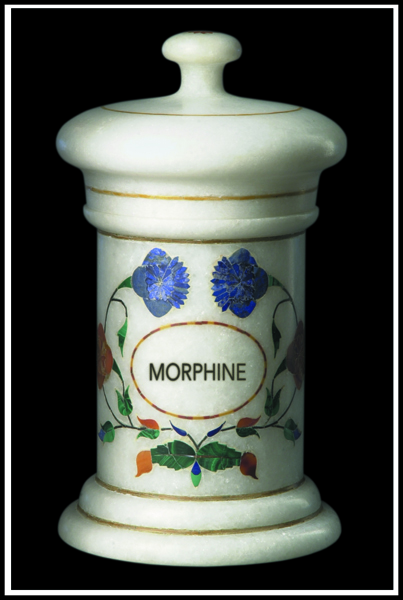 Of a white ceramic jar with a lid. The jar has a round base and a narrow neck. The lid is slightly domed and has a small knob on top. The body of the jar is decorated with a floral design in blue red and green colors. The word "MORPHINE" is written in a cursive font in the center of the design. The background is black making the jar stand out.