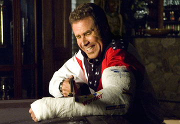 A man sitting at a bar with a big smile on his face. He is wearing a red and white jacket with the word "Wonder" written on it and has a bandage wrapped around his arm. The man appears to be in his late 40s or early 50s and has shoulder-length dark hair. He has a watch on his left wrist and is holding a cigarette in his right hand. The background is dark and there are bottles of alcohol on the shelves behind him. The overall mood of the image is happy and relaxed.