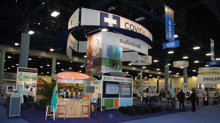 A trade show booth with a blue and white color scheme. The booth has a large banner that reads "COVIDIEN" in bold letters at the top. Below the banner there is a sign that says "Mallinckrodt 400" in smaller letters. <br /><br />In the center of the booth there are several smaller banners with images and text related to the virus. On the left side of the image there appears to be a counter with various items on display. In the background there seems to be another booth with more information about the virus and its effects on the environment.<br /><br />The booth is set up in a large hall with high ceilings and large windows. There are several people walking around the booth and a few people sitting at tables and chairs. The floor is covered in a blue carpet.