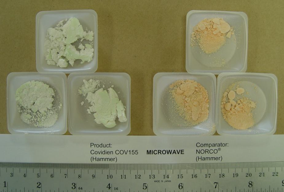 Six small plastic containers arranged in two groups of three on a beige background. All containers are holding a powdery substance. The three containers on the left have a white powder and are labeled "Product: Covidien COV155 (Hammer)" and the three containers on the right contain a pink powder and are labeled "Comparator: NORCO (Hammer)". The word "Microwave" is between the two labels. A ruler at the bottom of the image suggests scale.