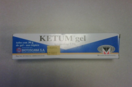 Of a white and blue box of Ketum gel. The box is rectangular in shape and has a blue and white label on the front. The label has the brand name "KETUM gel" written in bold black letters at the top followed by the product name "tubo com 30g de gel - uno topico" in smaller black letters. Below that there is a description of the product which reads "Biotoscana S.A." which translates to "Ketum gel" in English. On the right side of the label there are two logos - one is a red and white shield with a blue background and the other is a yellow and black shield with the letter "M" in the center. At the bottom right corner of the box it says "Made in Italy" in black letters indicating that the product is made in Italy.