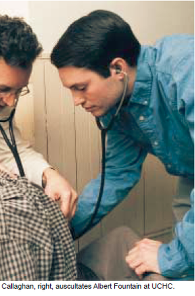 Two men one on the left and one in the middle examining a patient's chest with a stethoscope. The patient appears to be a young man with dark hair and is wearing a blue shirt. The doctor on the right is standing next to the patient wearing a white shirt and glasses. They are both looking down at the patient and appear to be focused on the patient. The background is a plain white wall. The image is likely taken in a medical office or clinic setting.