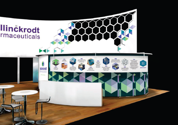 A trade show booth for Mallinckrodt Pharmaceuticals. The booth is white with a curved design and has a large banner at the top that reads "MALLINCKRODT PHARMACEUTICALS". Below the banner there is a large screen with a colorful geometric pattern in shades of blue green and purple. On the right side of the booth there are several smaller screens displaying information about the company's products and services. There are also two small tables and two chairs in front of the screen. The background is black and the booth is set up on a wooden floor.