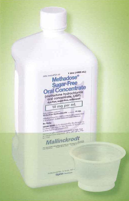 A white plastic bottle with a white cap. The bottle is labeled "Methadose Sugar-Free Oral Concentrate" and has a label that reads "10 mg per ml". Next to the bottle there is a small white plastic cup. The background is a light green color.