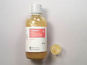 A small glass bottle with a white cap and a red label. The label has the brand name "Tessalon" written in bold black letters at the top followed by the product name "C" in smaller black letters. Below that there is a smaller label with the same brand name and product name. The bottle is filled with a light-colored liquid which appears to be a honey or honeycomb-like substance. Next to the bottle there are two small droplets of the same liquid one on the right side of the image. The background is plain white.