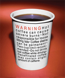 Of a white paper cup with black text on it. The text reads "WARNING HOT COFFEE CAN CAUSE SEVERE BURNS - NOT RESPONSIBLE FOR LOOSE FITTING LIDS. Coffee stains can be permanent. Two cup limit recom-mended. Do not drink hot coffee while driving. Decaffeinated coffee may contain slight amount of caffeine." The cup appears to be empty and is placed on a red background.