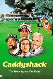 A DVD cover for the movie "Caddyshack: The Snobs Against The Slobs!" The cover features a group of four men standing in front of a large white building with a green lawn and trees in the background. The men are all wearing suits and hats and one of them is holding an orange flag with the number 19 on it. The title of the movie is written in bold yellow letters at the top of the cover and the DVD logo is in the bottom right corner.