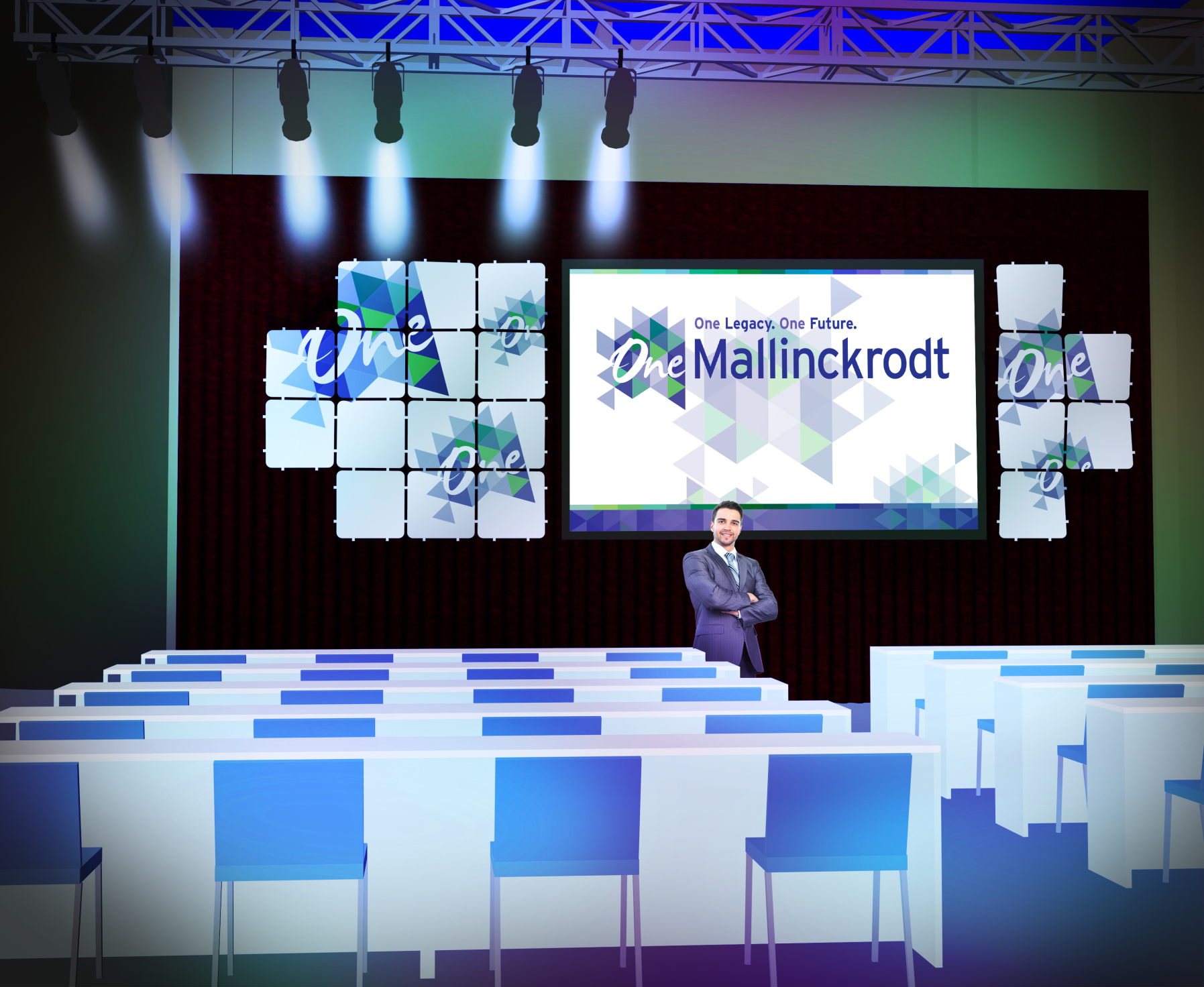 A stage set up for a presentation. The stage has a red curtain and a large screen with the text "One Mallinckrodt" on it. The screen is decorated with blue and white geometric shapes. On the right side of the stage there is a man standing in front of the screen with his arms crossed. He is wearing a suit and tie and appears to be giving a speech or presentation. There are rows of blue chairs on either side of him and the stage is lit up with spotlights. The overall color scheme of the image is blue white and green.