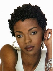 A close-up portrait of a young Black woman. She is wearing a white tank top and large hoop earrings. Her hair is curly and short. She has a serious expression on her face and is looking directly at the camera. The background is plain white making the woman the focal point of the image.