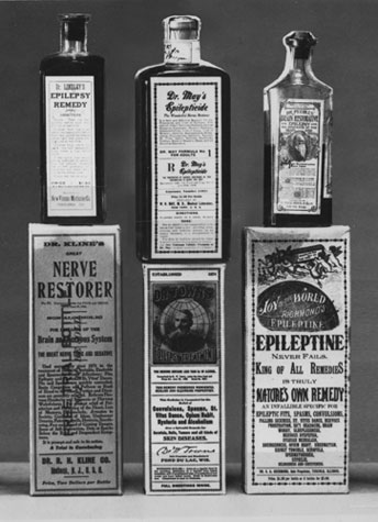 A group of six bottles of medicine arranged in a pyramid-like formation. All the bottles appear to be old and worn with some of the labels showing signs of wear and tear. <br /><br />The first bottle on the top left is labeled "Nerve Restorer" and has a label that reads "Dr. R. E. Ellington's Nerve Restorer". The second bottle is labeled "Epileptine" and is labeled as "King of All Remedies". The third bottle is titled "Natures Own Remedy" and contains a label with an illustration of a man's face and the words "World Epilepticine". The fourth bottle has a description which states that it is "King-of-All Remedy". The fifth bottle has an image of a woman's face and the sixth bottle has the same label as the first bottle.<br /><br />The background is plain and the overall color scheme of the image is black and white.