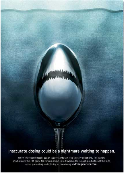 A digital art piece that features a spoon with a shark's mouth on it. The spoon is in the center of the image with the mouth open wide revealing sharp teeth. The background is a dark blue color and the spoon is positioned in the middle of the frame. The text on the image reads "Inaccurate dosing could be a nightmare waiting to happen." Smaller text underneath reads "When improperly dosed cough suppressants can lead to scary situations. This is part of what gave the FDA cause for concern about liquid hydrocodone cough products. Get the facts about underdosing or overdosing at dosingmatters.com." The text is written in white and is in a modern sans-serif font. The overall tone of the piece is dark and ominous conveying a sense of fear and uncertainty.