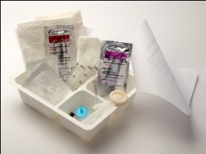 A white plastic tray with various medical supplies inside. On the left side of the tray there are two packets of bandages one with a red label and the other with a white label. Next to the packets there is a small plastic container with a blue lid and a white handle. On top of the container there appears to be a small syringe with a needle inserted into it. The syringe is resting on a piece of white paper. The background is plain white.