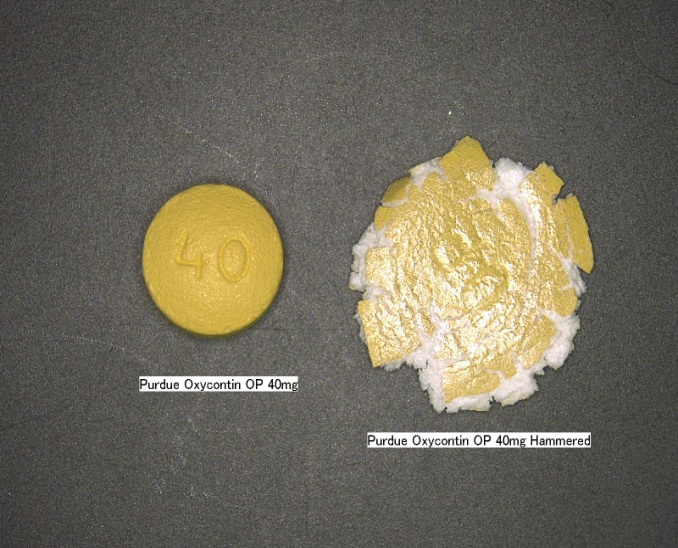 A yellow pill with the number 40 on it lying on a black surface. The pill is labeled "Purdue Oxycontin OP 40 mg". Next to the pill there is what appears to be a second pill that has been flattened. The second pill is labeled "Purdue Oxycontin OP 40 mg Hammered".