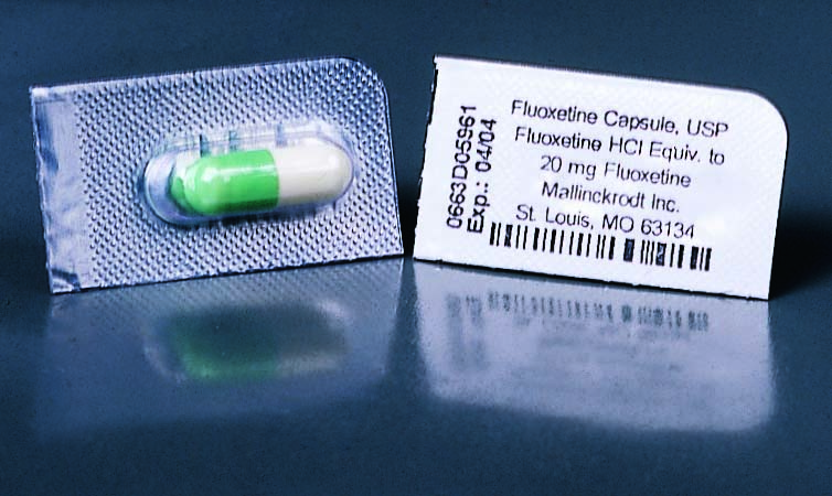 A blister pack of Fluoxetine Capsule USP with a label on it. The blister pack is silver in color and has a green and white capsule inside. The label on the blister pack reads "Fluoxetine Capsule USP" and "20 mg HCI Equiv. to Mallinckrodt Inc. St. Louis MO 63134". The label also has a barcode and some information about the product. The background is black and the blister packs are placed on a reflective surface.