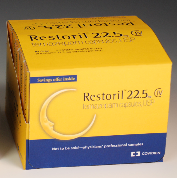 Of a yellow box of Restoril 22.5 mg tablets. The box is rectangular in shape and has a blue label on the front. The label has the brand name "Restoril" written in bold black letters at the top followed by "22.5" in smaller black letters. Below that there is a description of the product which states that it is a temazepam capsule with USP and "Not to be sold-physicians' professional samples". The box also has a small illustration of a crescent moon on the bottom right corner. The background of the box is plain white.