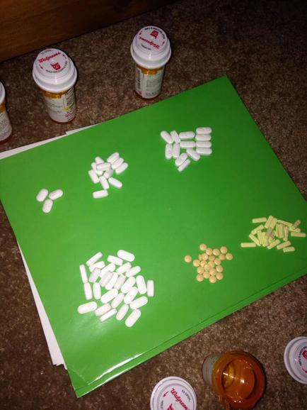 A green cutting board with several white pills scattered on it. The pills are of different sizes and shapes and they are arranged in a scattered manner. On the left side of the cutting board there are several prescription bottles with white lids and on the right side there is a small orange bottle with a white lid. The background is a brown countertype.
