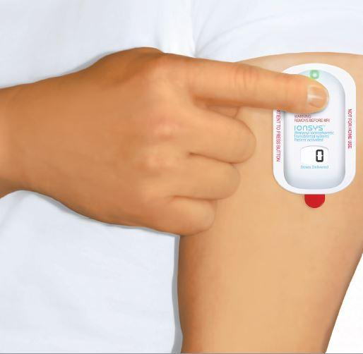 A person's arm with a blood pressure monitor attached to it. The monitor is white in color and has a red button on the right side. The person's hand is pointing towards the monitor. On the left side of the image there is a label that reads "Blood Pressure Monitor". The background is plain white.