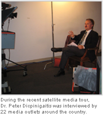 A man sitting in a chair in a room with a white wall and a light fixture in the background. He is wearing a suit and tie and appears to be in the middle of a conversation. On the left side of the image there is a camera and a video camera on a tripod. The text on the image reads "During the recent satellite media tour Dr. Peter Dicpinigaitis was interviewed by 22 media outlets around the country."