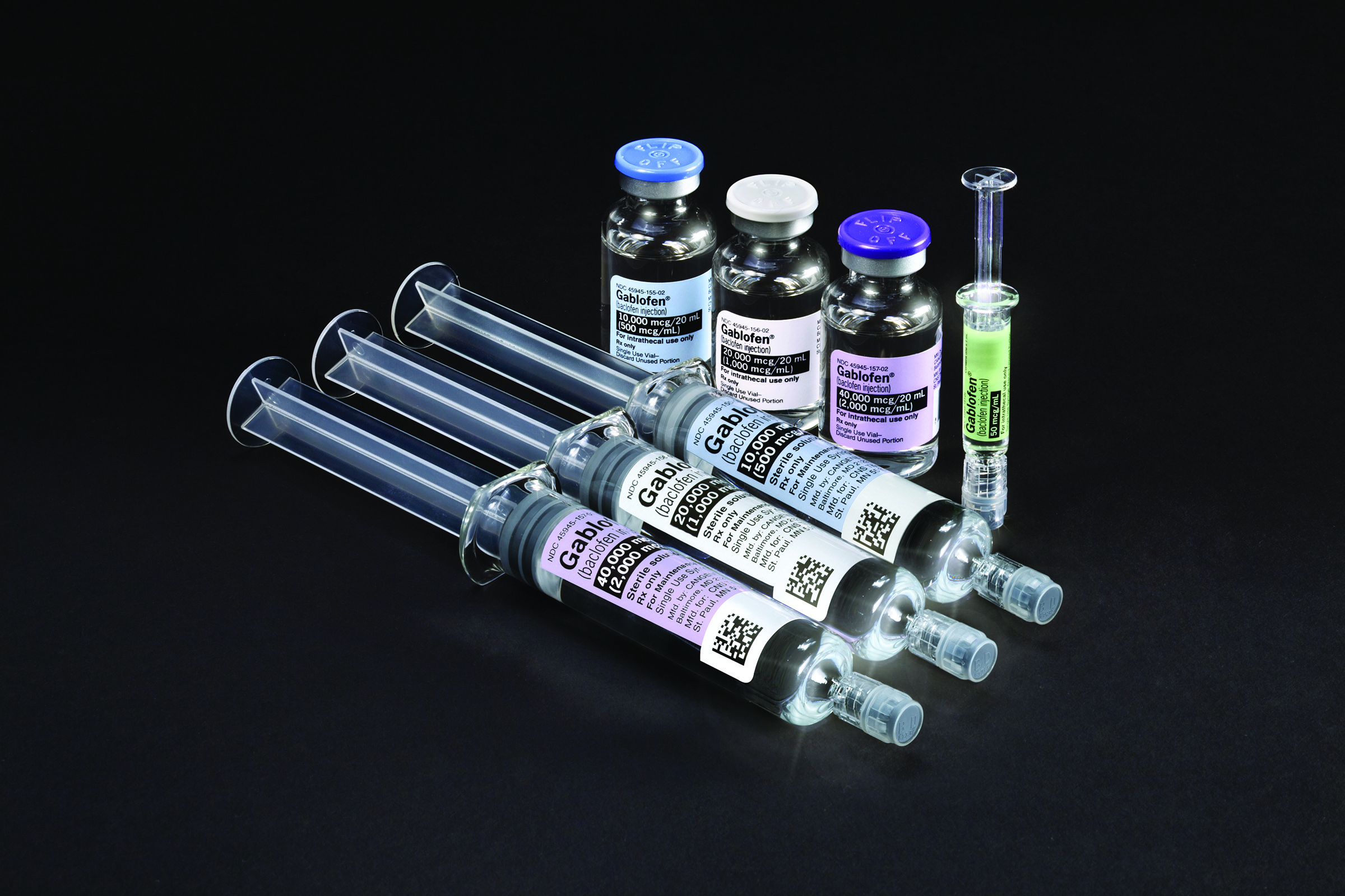 A group of six syringes arranged in a row on a black background. There are six vials of different sizes and shapes each with a blue cap and a white label. The vials are filled with different colored liquids including black purple and green. There is also a small syringe with a green liquid in it. The syringe appears to be filled with a clear liquid possibly a vaccine or a similar substance. The background is completely black making the syringe and vials stand out.