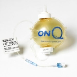 A yellow-colored medical device with a white pump attached to it. The device has a label on it that reads "ONQ Ask Your Surgeon.com". The label also has a barcode and some information about the device. There is also a blue-colored syringe attached to the device.