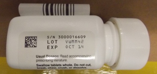 A white pill bottle with a white cap. The label on the bottle reads "S/N 300016609 LOT EXP OCT 14". There is also a barcode and a QR code on the label. The bottle appears to be lying on a yellow surface.