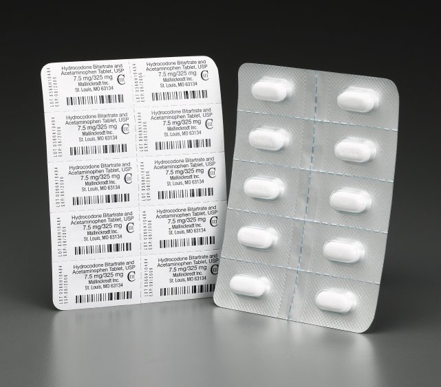 A blister pack of white pills. The blister pack is rectangular in shape and has multiple rows of small white pills arranged in a grid-like pattern. On the left side of the blister pack there is a white label with black text and barcodes. The label appears to be a list of ingredients and nutritional information. The background is black making the white pills stand out.